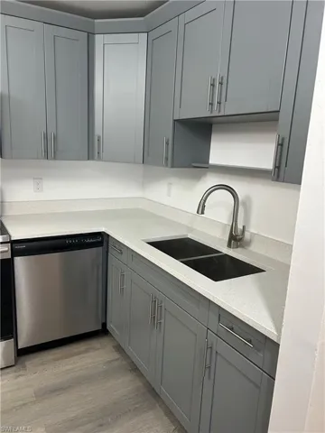 Kitchen featuring gray cabinetry, dishwasher, light wood-style floors, and light stone counters