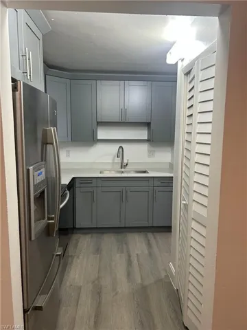 Kitchen with stainless steel fridge, gray cabinets, dark wood-type flooring, and light stone counters