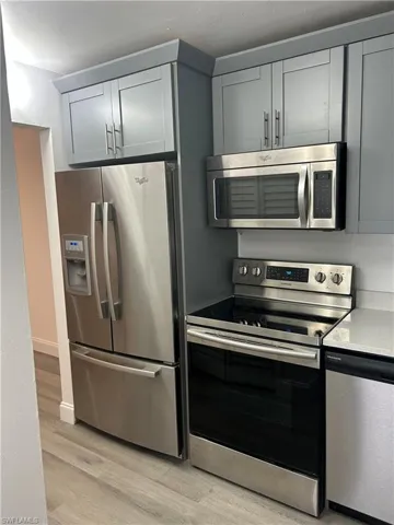 Kitchen with appliances with stainless steel finishes, gray cabinetry, light wood-type flooring, and light stone counters