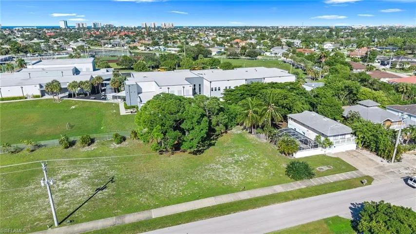 Aerial perspective of property featuring an expansive grass lawn, mature trees, and an attached screened-in patio area