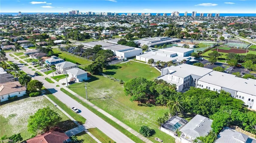 Aerial perspective featuring a level parcel of land, proximity to established paved thoroughfares, mature trees, and surrounding coastal infrastructure