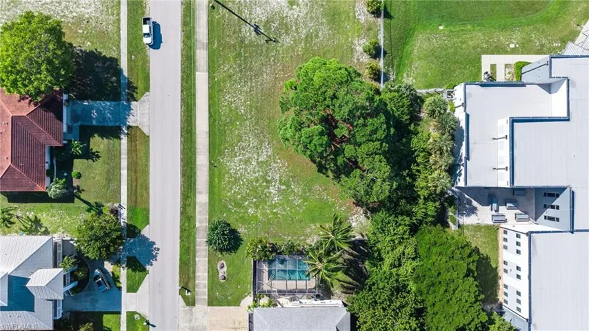 Aerial view of the vacant parcel featuring established shade trees, direct street access, and a clear building site