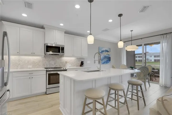 Kitchen with stainless steel appliances, light wood-type flooring, an island with sink, a kitchen breakfast bar, and white cabinets