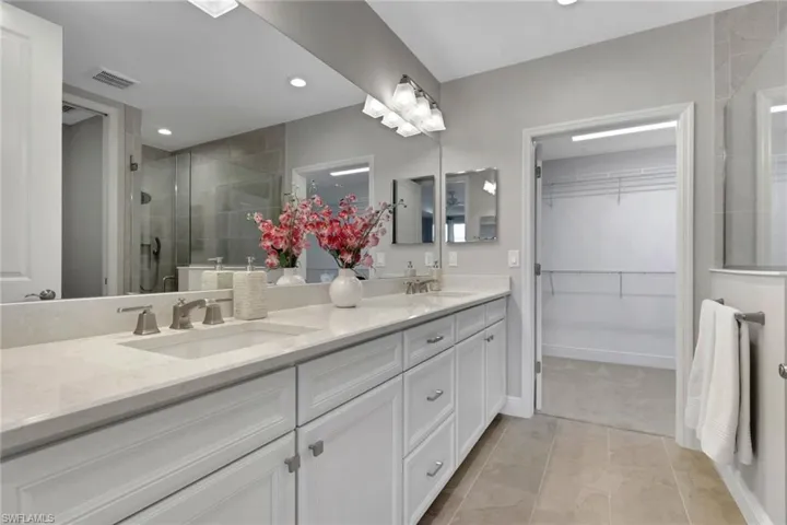 Full bathroom with a shower stall, double vanity, a spacious closet, light tile patterned flooring, and recessed lighting