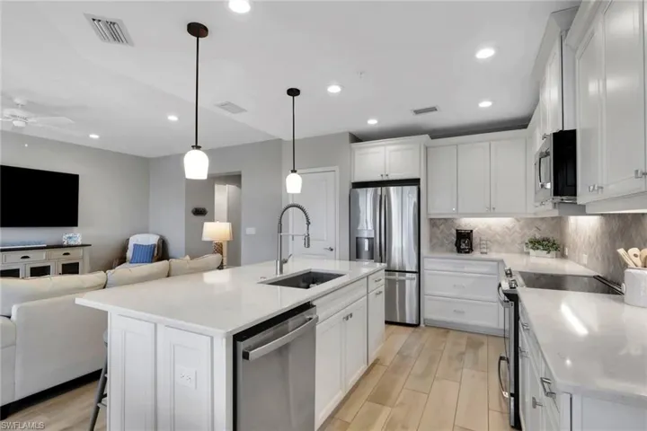 Kitchen featuring open floor plan, a breakfast bar, stainless steel appliances, wood tiled floors, and white cabinets