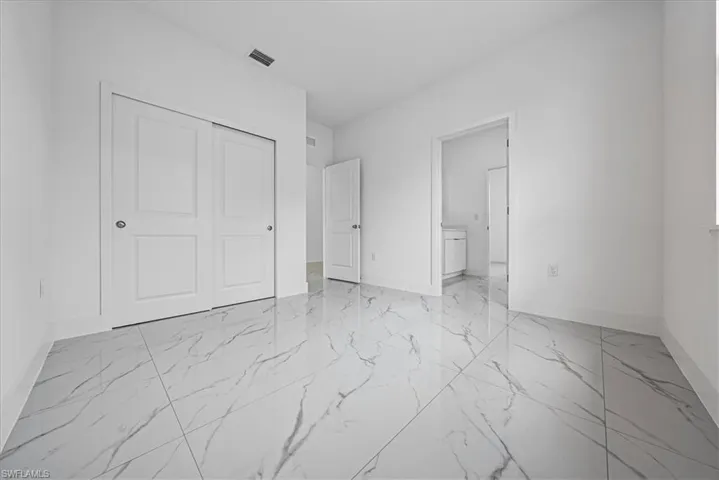 Unfurnished bedroom featuring light marble finish floors, a closet, and ensuite bathroom