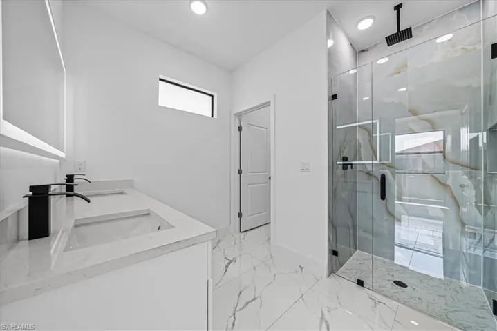 Bathroom featuring double vanity, a marble finish shower, recessed lighting, and light marble finish floors