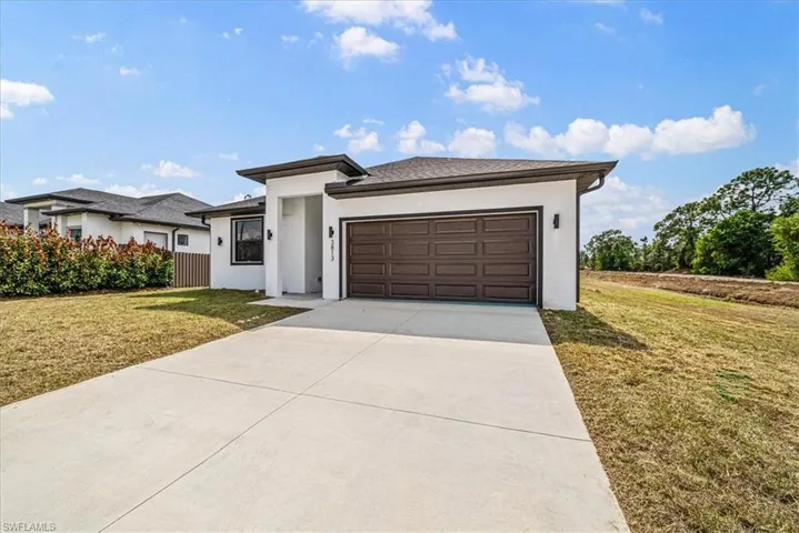 Prairie-style home with a front lawn, an attached garage, stucco siding, and driveway