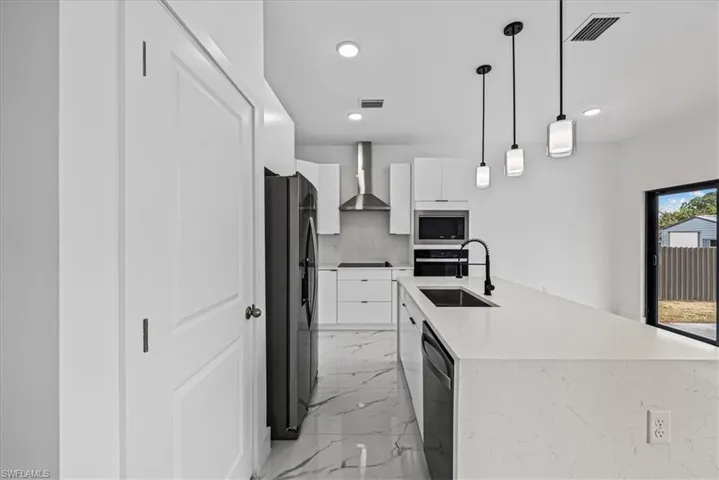 Kitchen with white cabinetry, modern cabinets, light marble finish flooring, light stone countertops, and black appliances
