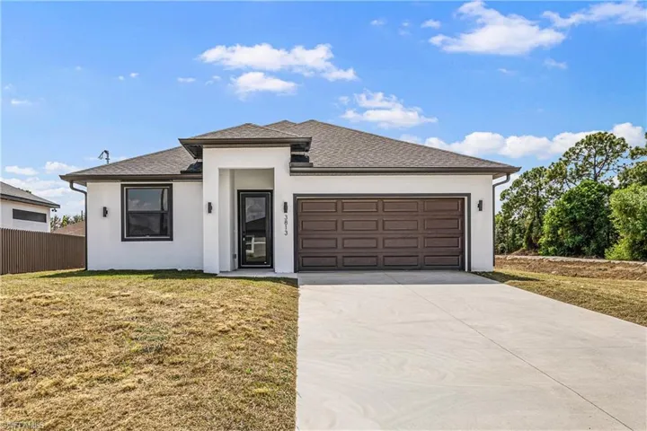 View of front of house featuring an attached garage, a front lawn, driveway, stucco siding, and a shingled roof