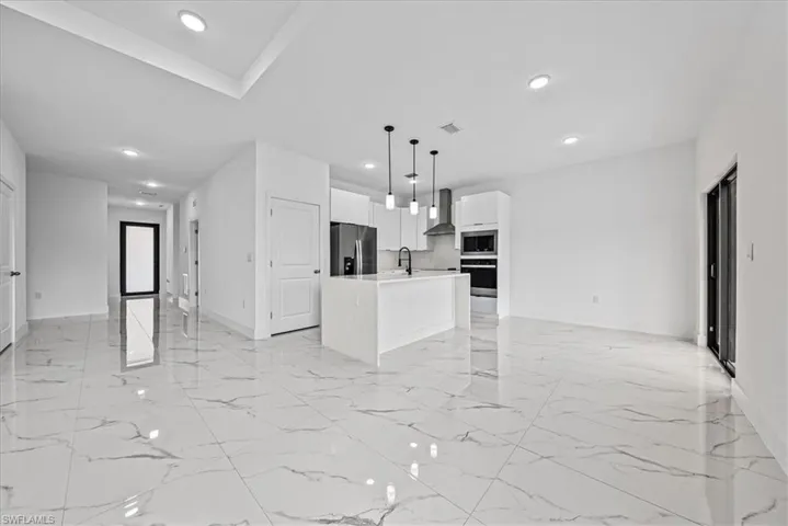 Kitchen featuring open floor plan, hanging light fixtures, an island with sink, and white cabinetry