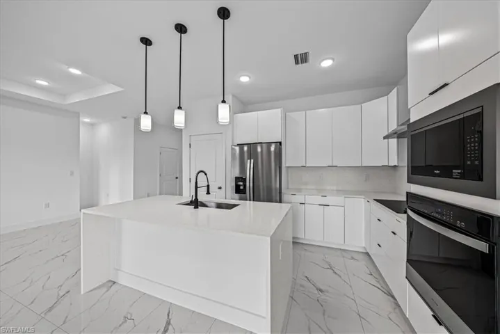 Kitchen featuring black appliances, light stone countertops, an island with sink, and modern cabinets