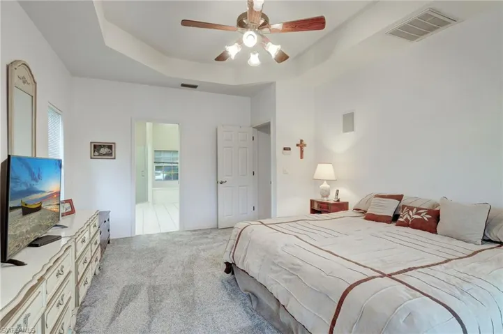 Carpeted bedroom with a tray ceiling, ensuite bathroom, and ceiling fan