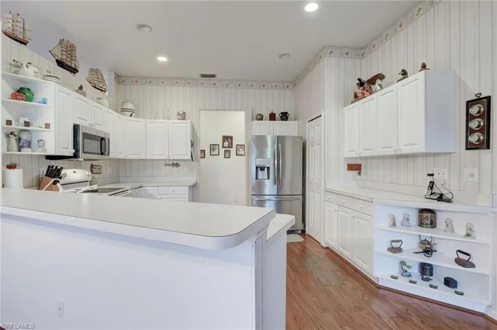 Kitchen with light hardwood / wood-style floors, kitchen peninsula, tasteful backsplash, white cabinetry, and appliances with stainless steel finishes