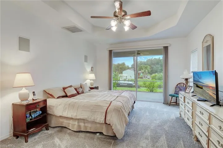 Carpeted bedroom with ceiling fan, a raised ceiling, and access to exterior
