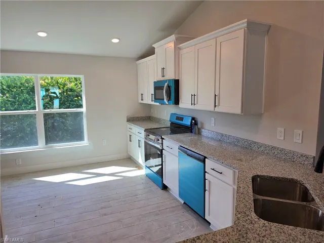 Kitchen featuring white cabinetry, stone-finish countertops, stainless steel dual-basin sink, recessed lighting, and wood-finish flooring