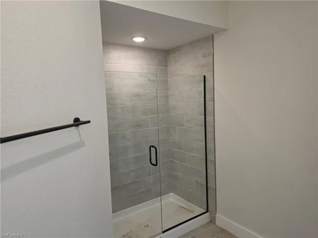 Walk-in shower featuring grey subway-style wall tile, a frameless glass door with black hardware, recessed ceiling lighting, and a black wall-mounted towel bar