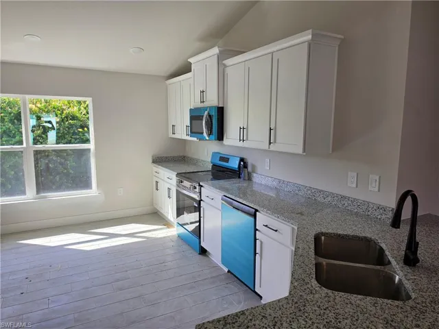 Kitchen featuring white shaker-style cabinetry, stone-finish countertops, dual-basin stainless steel sink with a matte black faucet, and light-tone plank flooring