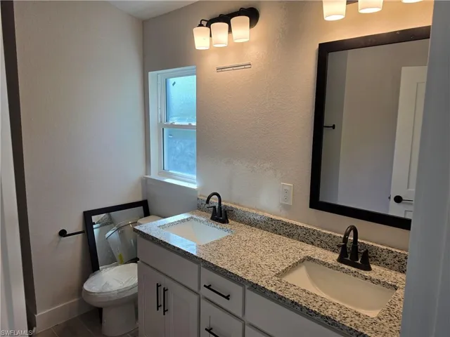 Dual-sink vanity with stone-finish countertop, white cabinetry with dark hardware, framed mirror, and multi-light fixtures