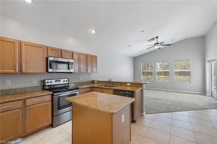 Kitchen featuring lofted ceiling, ceiling fan, light tile floors, and stainless steel appliances