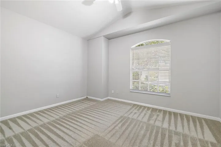 Carpeted empty room with a wealth of natural light, ceiling fan, and lofted ceiling