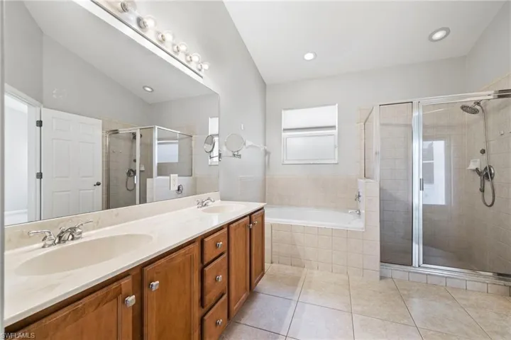 Bathroom featuring tile flooring, vanity with extensive cabinet space, separate shower and tub, and double sink