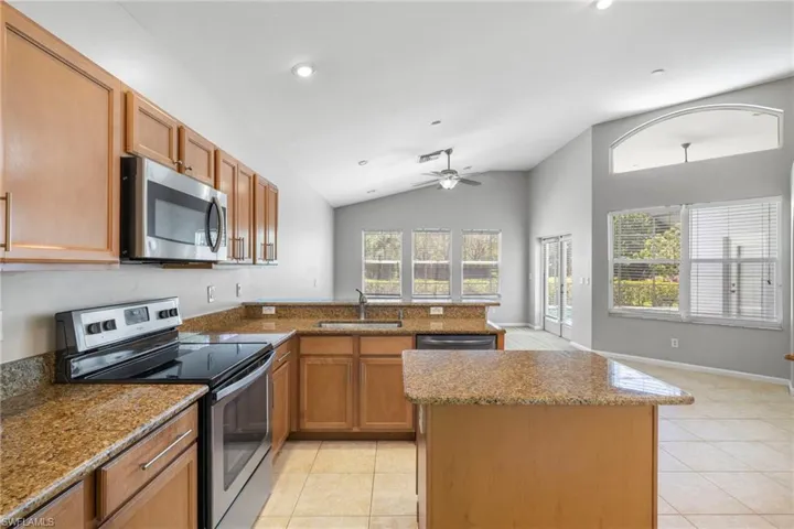 Kitchen with appliances with stainless steel finishes, sink, light tile flooring, ceiling fan, and vaulted ceiling