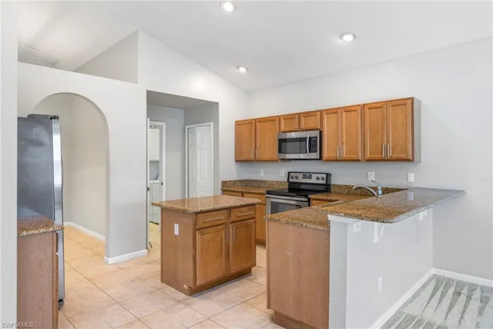 Kitchen featuring stainless steel appliances, light carpet, kitchen peninsula, stone counters, and vaulted ceiling