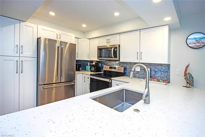 Kitchen featuring light stone counters, a sink, decorative backsplash, stainless steel appliances, and white cabinets