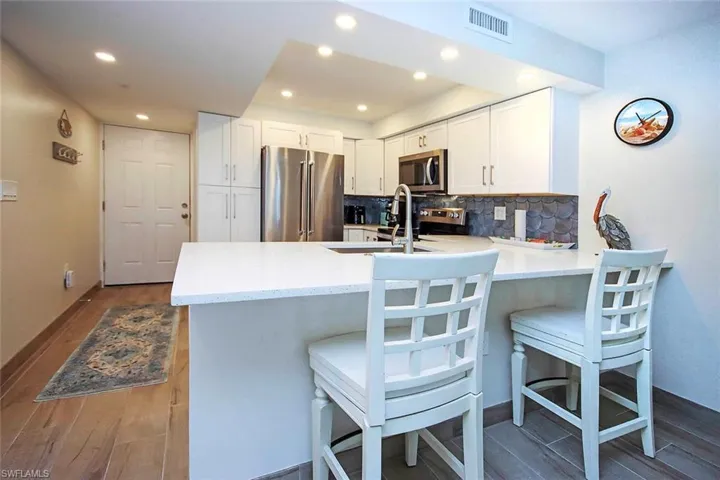 Kitchen featuring a peninsula, dark wood-type flooring, white cabinets, appliances with stainless steel finishes, and tasteful backsplash