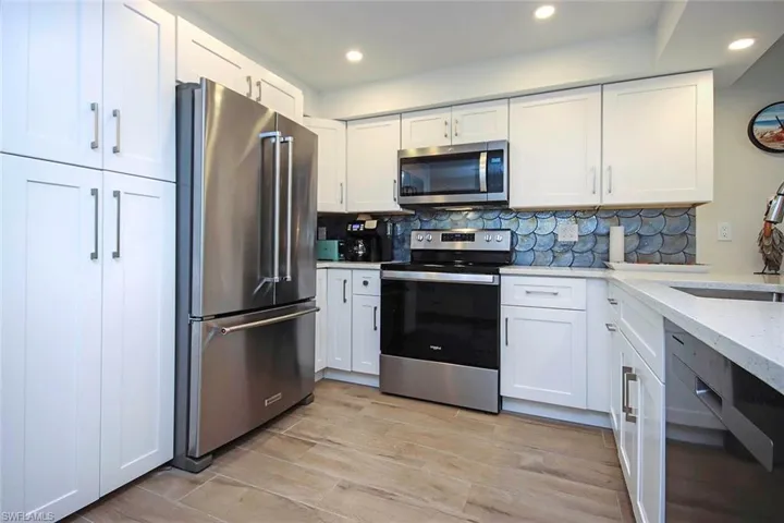 Kitchen with backsplash, appliances with stainless steel finishes, white cabinetry, and a sink