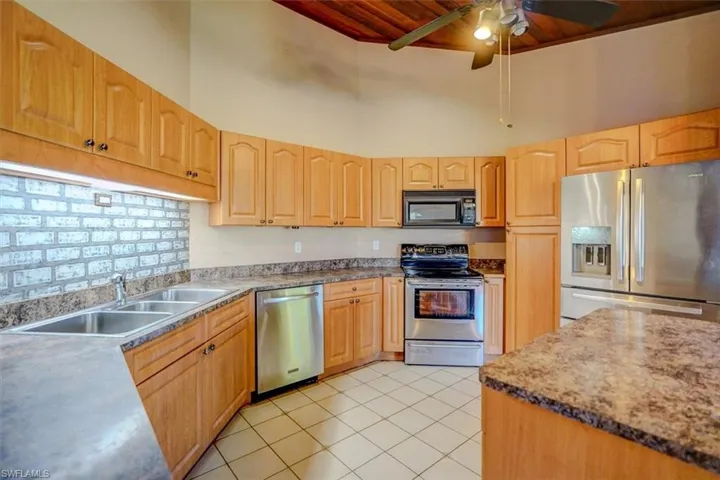 Kitchen featuring a high ceiling, ceiling fan, sink, stainless steel appliances, and light tile patterned floors