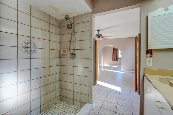 Bathroom with tile patterned flooring, a tile shower, vanity, and ceiling fan