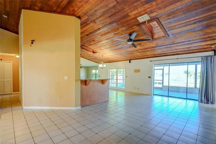 Empty room featuring lofted ceiling, wood ceiling, light tile patterned floors, and ceiling fan