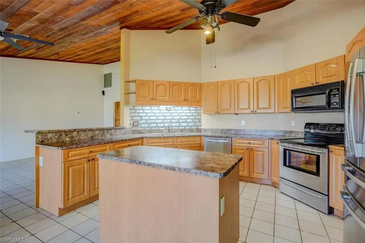 Kitchen with light brown cabinets, stainless steel appliances, wooden ceiling, and a center island