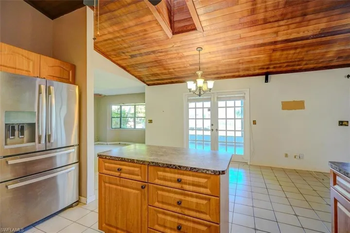 Kitchen with wooden ceiling, vaulted ceiling with skylight, hanging light fixtures, stainless steel fridge with ice dispenser, and light tile patterned floors