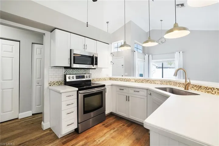 Kitchen with sink, hardwood / wood-style floors, appliances with stainless steel finishes, and decorative light fixtures