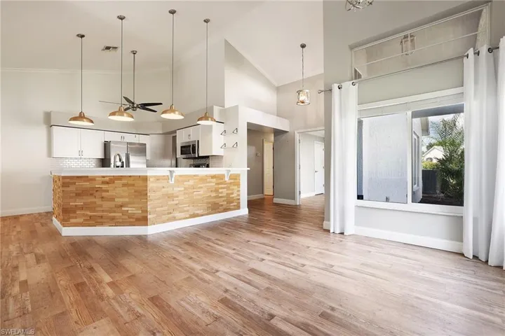 Kitchen featuring appliances with stainless steel finishes, high vaulted ceiling, decorative light fixtures, and white cabinets