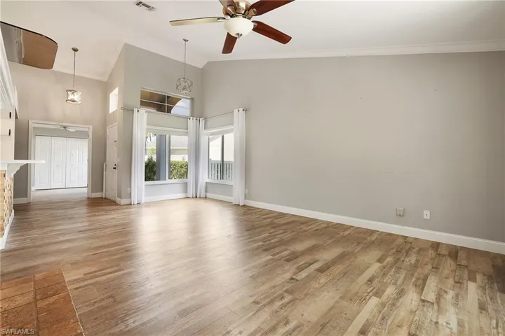 Unfurnished living room featuring ornamental molding, ceiling fan with notable chandelier, a towering ceiling, and light hardwood / wood-style floors