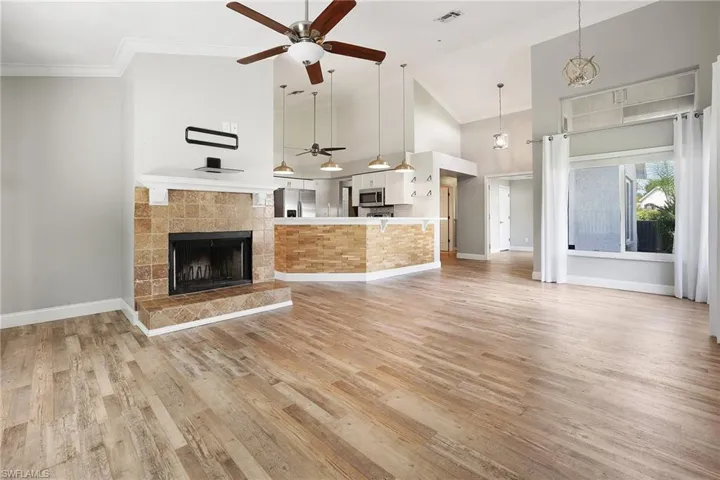 Unfurnished living room featuring a tile fireplace, crown molding, light hardwood / wood-style floors, ceiling fan, and high vaulted ceiling
