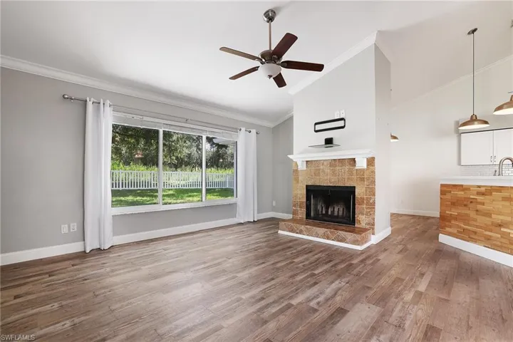 Unfurnished living room featuring a tiled fireplace, crown molding, hardwood / wood-style floors, ceiling fan, and high vaulted ceiling