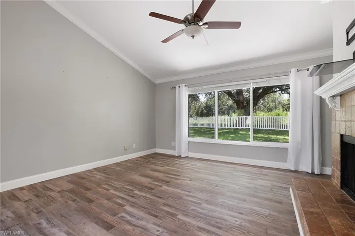 Unfurnished living room with a tiled fireplace, dark wood-type flooring, crown molding, lofted ceiling, and ceiling fan