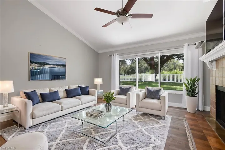 Living room with dark wood-type flooring, a tiled fireplace, high vaulted ceiling, ornamental molding, and ceiling fan