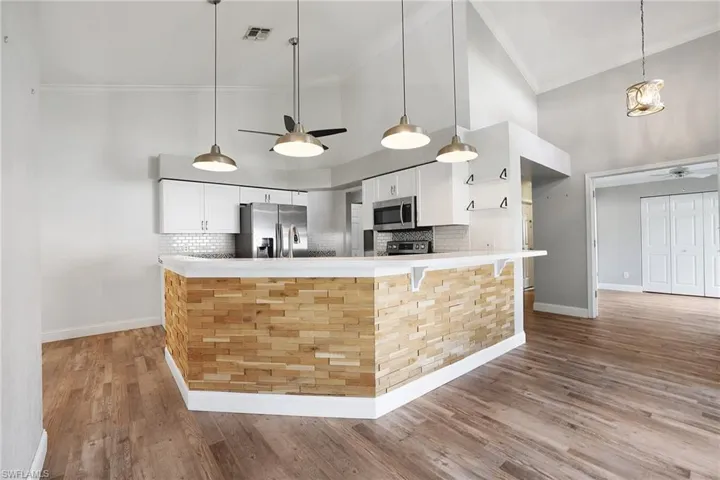 Kitchen featuring decorative light fixtures, wood-type flooring, ceiling fan, appliances with stainless steel finishes, and white cabinets