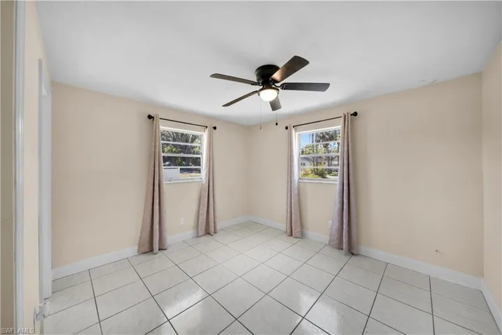 Unfurnished room featuring a ceiling fan, light tile patterned flooring, baseboards, and a wealth of natural light