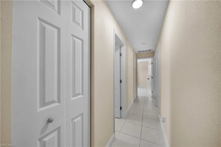 Hallway with baseboards, visible vents, and light tile patterned floors