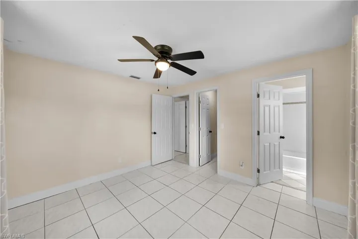 Unfurnished bedroom with light tile patterned floors, baseboards, connected bathroom, visible vents, and a ceiling fan
