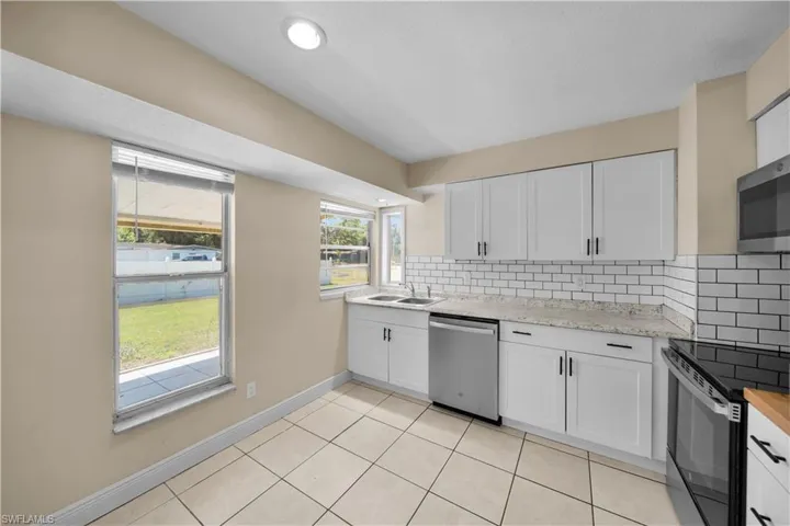 Kitchen with white cabinets, appliances with stainless steel finishes, a sink, backsplash, and light tile patterned floors