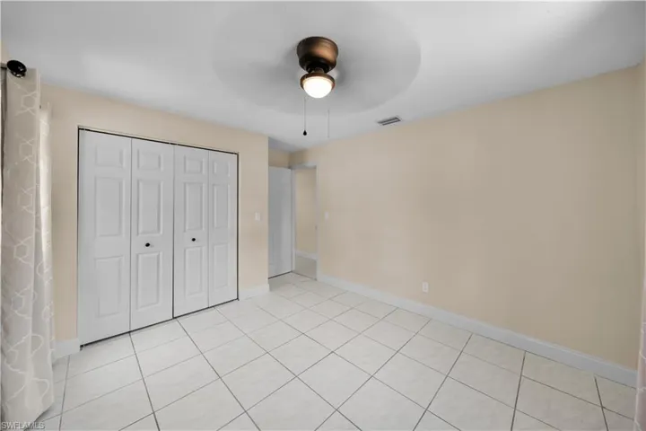 Unfurnished bedroom with light tile patterned floors, baseboards, ceiling fan, visible vents, and a closet