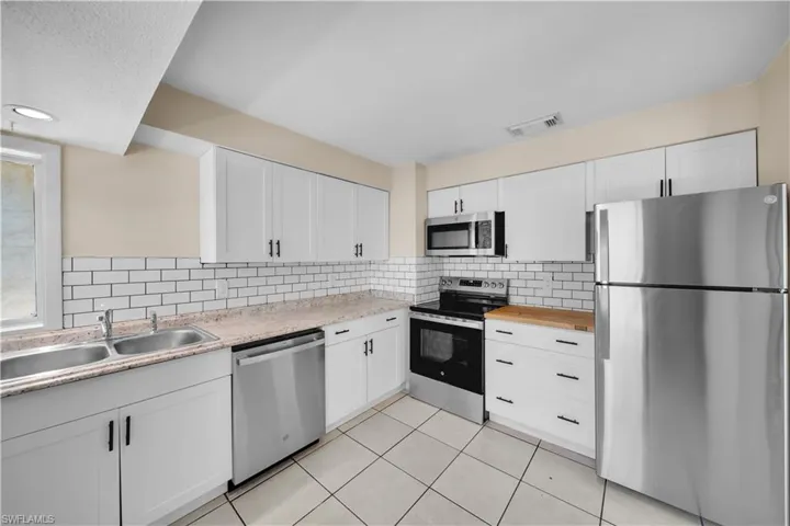 Kitchen featuring white cabinetry, stainless steel appliances, decorative backsplash, a sink, and visible vents
